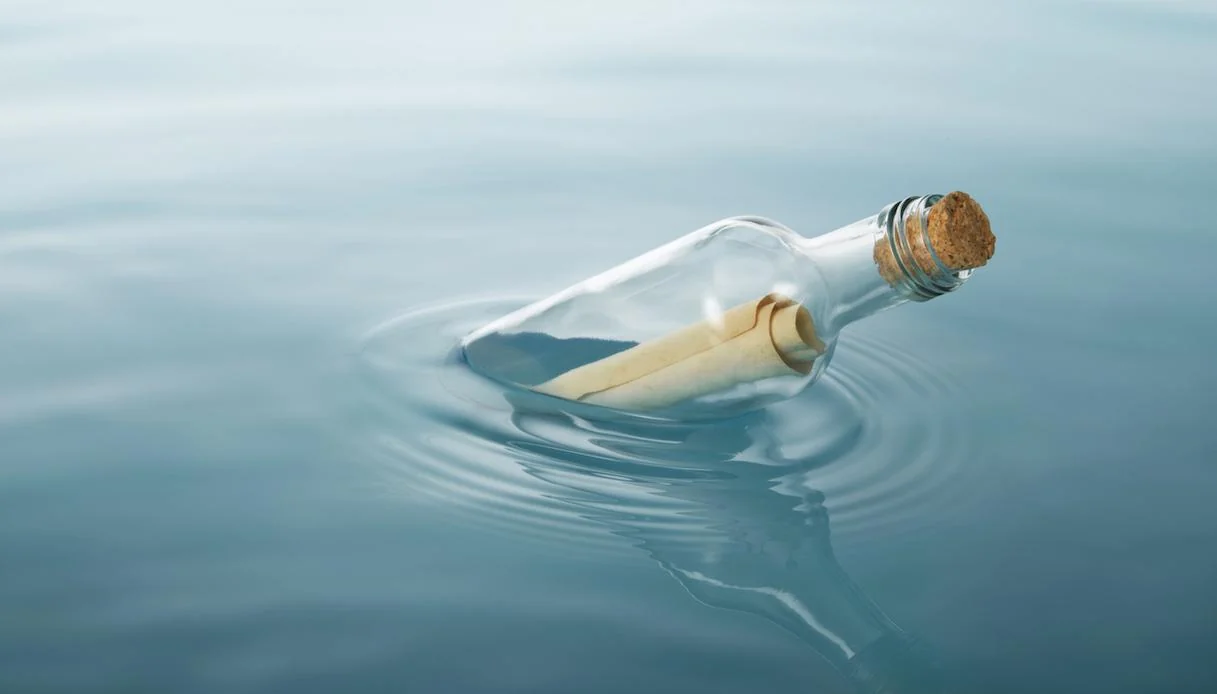 静かな湖面に浮かぶ手紙入りのガラス瓶